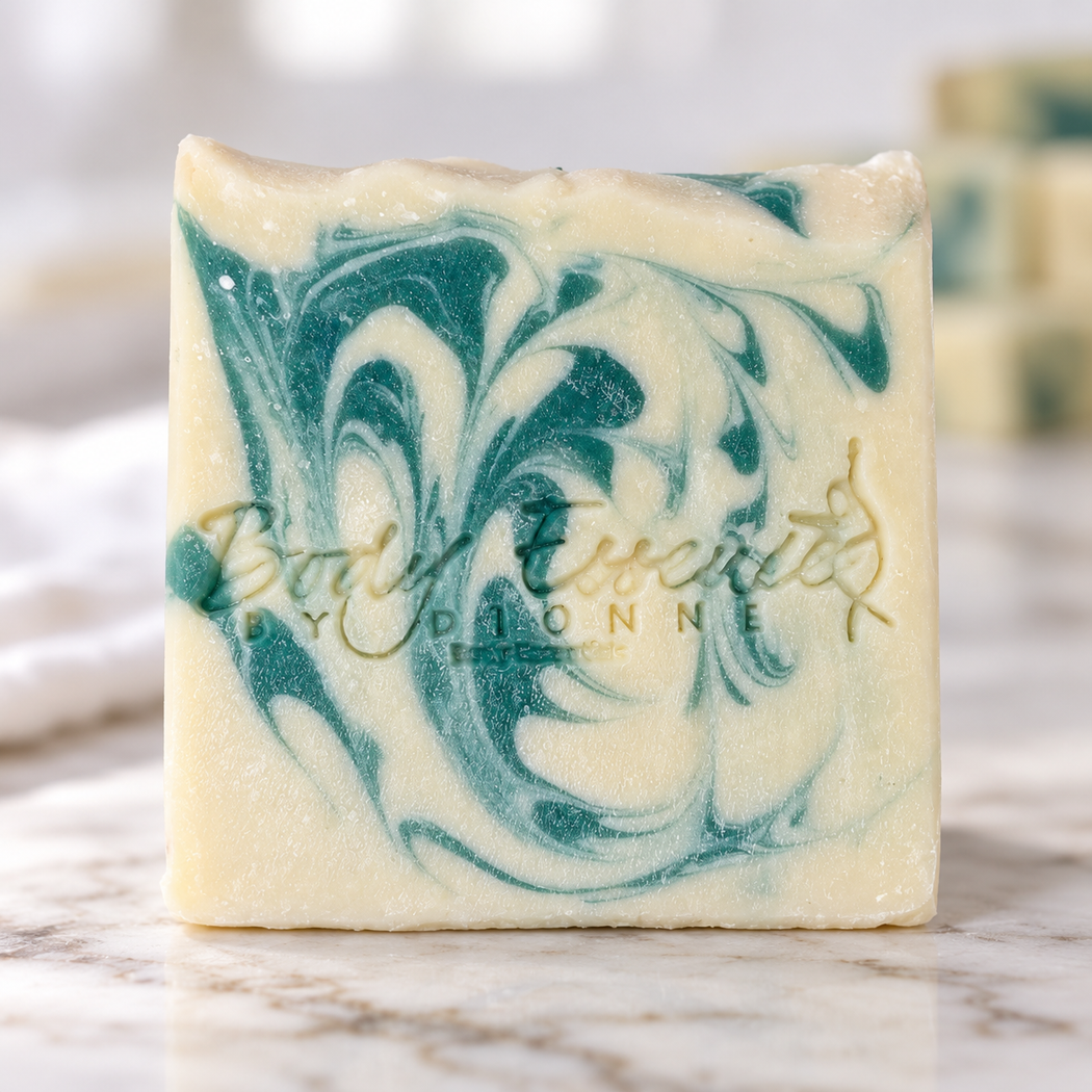 Handmade Sunday Linen soap bar with a teal swirl and the Body Essence by Dionne logo stamped into the top, on white marble